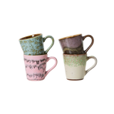 Four small ceramic mugs with speckled and drip-style glazes, stacked in two pairs on a plain white background. One mug is light green, one is pink, one is mauve-brown, and one is cream with green speckles.