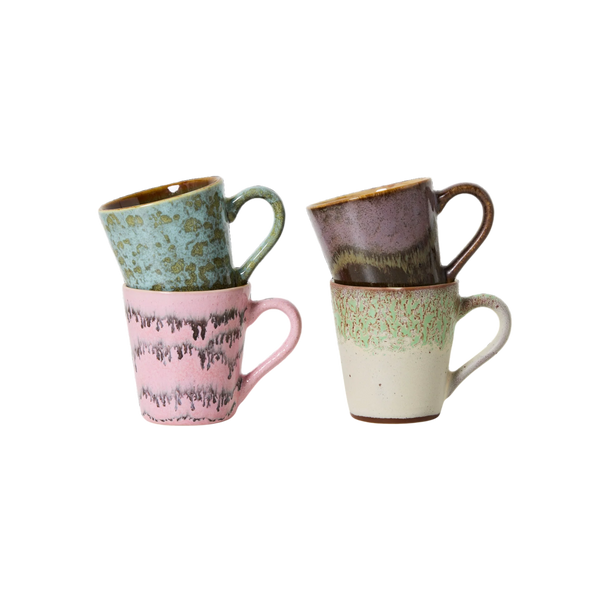 Four small ceramic mugs with speckled and drip-style glazes, stacked in two pairs on a plain white background. One mug is light green, one is pink, one is mauve-brown, and one is cream with green speckles.