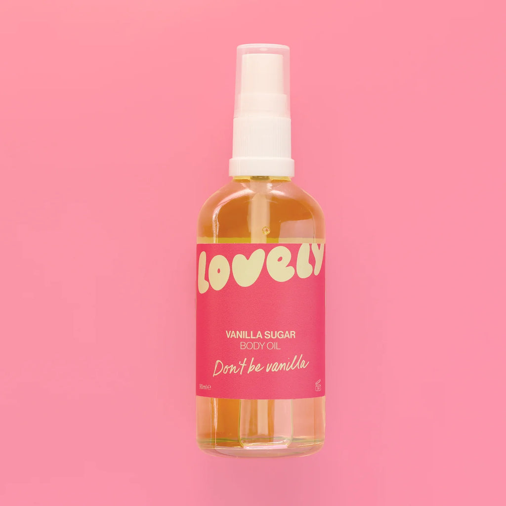 A bottle of Lovely Vanilla Sugar Body Oil with a pink label and white spray top, centered against a solid pink background.
