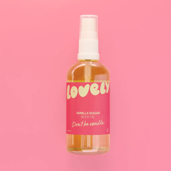 A bottle of Lovely Vanilla Sugar Body Oil with a pink label and white spray top, centered against a solid pink background.