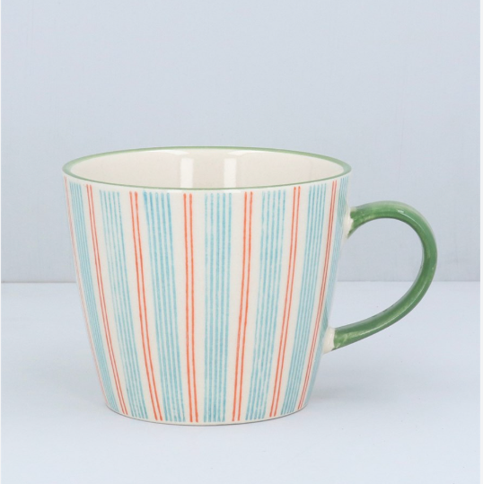 A ceramic mug with a cream-colored interior and exterior, decorated with vertical stripes in light blue and coral red, featuring a solid green handle.
