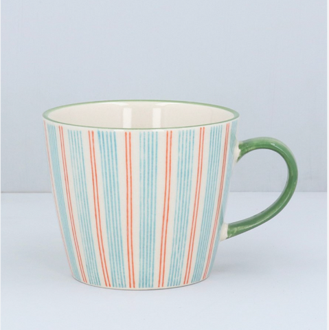 A ceramic mug with a cream-colored interior and exterior, decorated with vertical stripes in light blue and coral red, featuring a solid green handle.