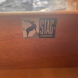 A close-up of a wooden furniture piece showing a metal brand plaque that reads 'STAG FURNITURE' with a stag silhouette logo.