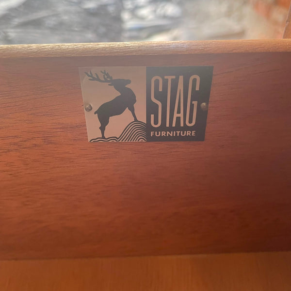 A close-up of a wooden furniture piece showing a metal brand plaque that reads 'STAG FURNITURE' with a stag silhouette logo.