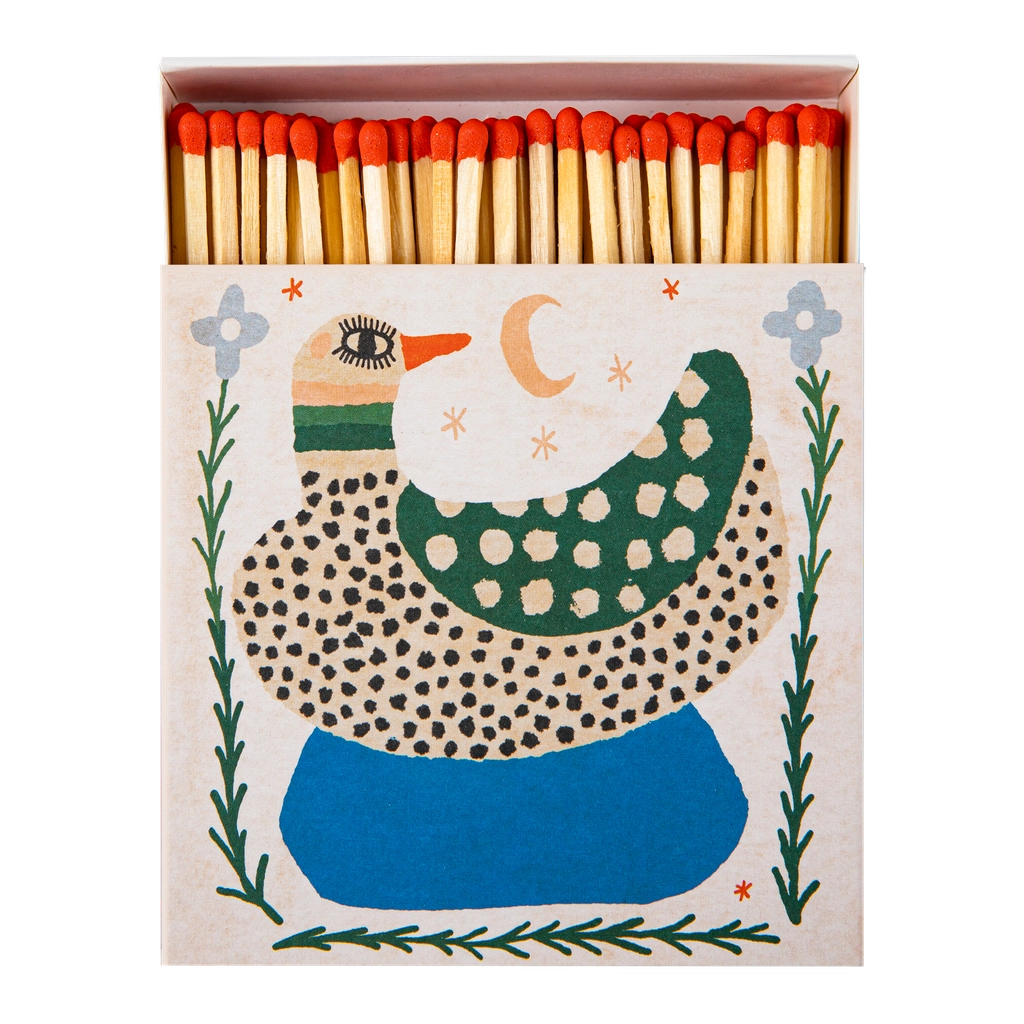 A decorative matchbox filled with wooden matches topped with red tips. The front of the box features a whimsical duck illustration in green, blue, black, and cream on a light beige background.
