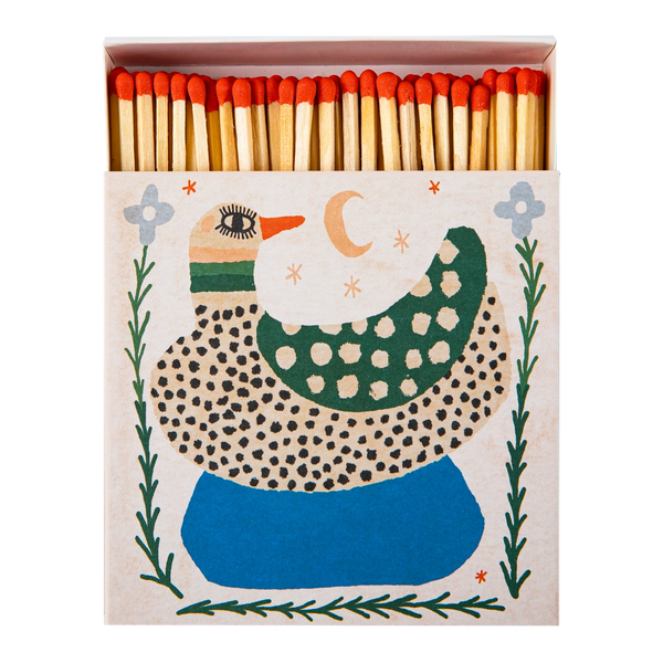 A decorative matchbox filled with wooden matches topped with red tips. The front of the box features a whimsical duck illustration in green, blue, black, and cream on a light beige background.