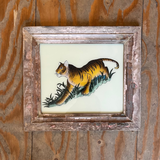 A framed vintage-style illustration of a tiger walking on grass, mounted on a rustic wooden plank wall.