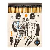 A matchbox filled with wooden matches, shown from above on a white background. The matchbox cover is cream-colored with a black line-art illustration of two riders on a spotted animal, accented with small orange and blue details.