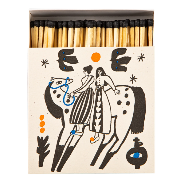 A matchbox filled with wooden matches, shown from above on a white background. The matchbox cover is cream-colored with a black line-art illustration of two riders on a spotted animal, accented with small orange and blue details.