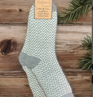 A pair of Jaspers taupe and white herringbone patterned men's socks hung on a wooden surface with Christmas decorations in the background.
