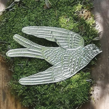 A silver metal swallow ornament with textured detailing, displayed on a bed of green moss over a rustic wooden surface.