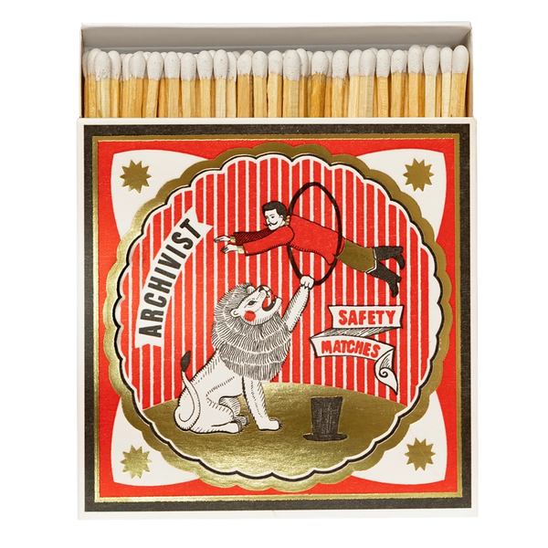 A vintage-style matchbox with wooden matches visible at the top and a illustrated front label reading 'ARCHIVIST' and 'SAFETY MATCHES.' The label shows a red-and-white striped circus scene with a lion and a person in a red outfit.