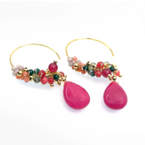 Annabella Moore Handcrafted Gemstone and Crystal 18k Gold plated earrings in dyed ruby. A pair of gold hoop earrings with dangling teardrop-shaped bright pink gemstones and clusters of small multicolored beads, shown on a clean white background.