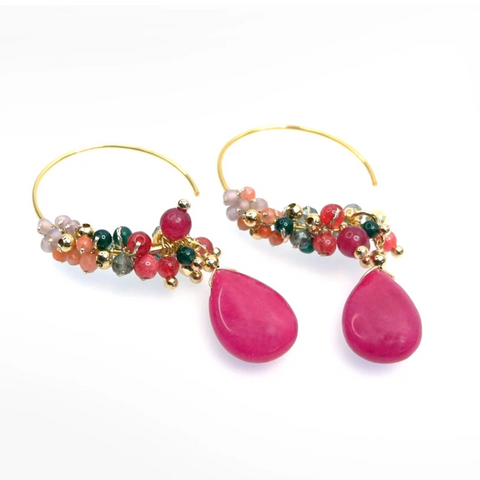 Annabella Moore Handcrafted Gemstone and Crystal 18k Gold plated earrings in dyed ruby. A pair of gold hoop earrings with dangling teardrop-shaped bright pink gemstones and clusters of small multicolored beads, shown on a clean white background.