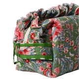 A quilted fabric storage bag with a green background and a red, blue, and white floral pattern, featuring a drawstring closure and a front pocket with green trim.