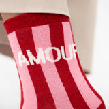 Red and pink striped sock with 'AMOUR' text on a neutral background