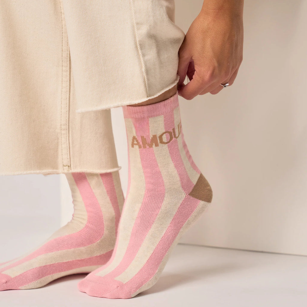 Pink and beige striped socks with 'AMOUR' text worn by a person.