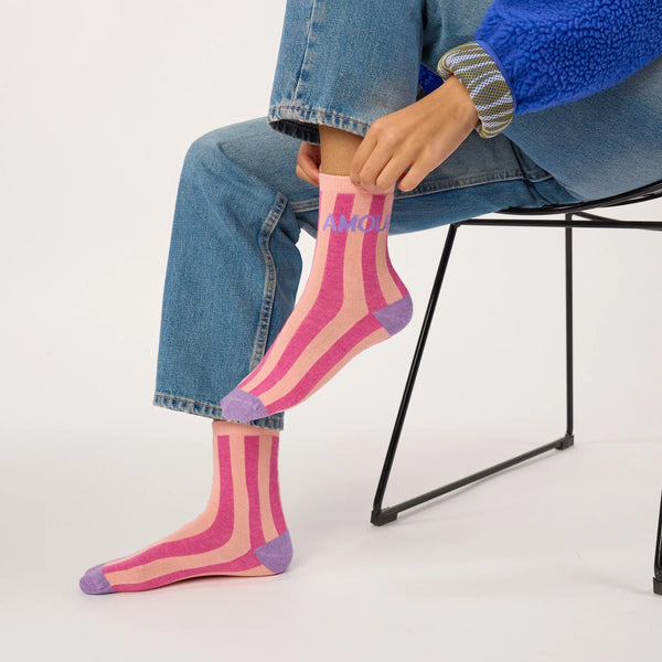 Person wearing colorful striped socks with 'AMOUR' text, sitting on a chair.