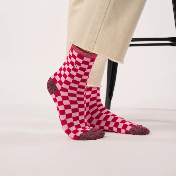 Red and white checkered crew socks worn with beige trousers, shown on a model's feet against a clean white studio background.