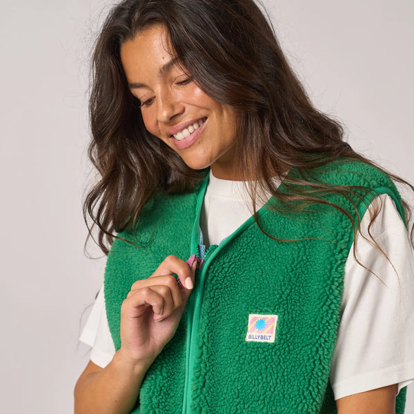 Woman wearing a green fleece vest with a visible brand logo on a plain background