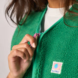 Person wearing a green fleece jacket with a colorful patch on a plain background