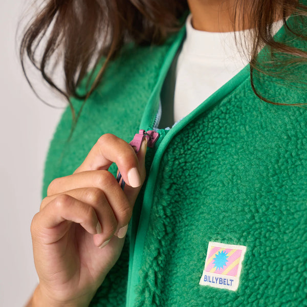 Person wearing a green fleece jacket with a colorful patch on a plain background