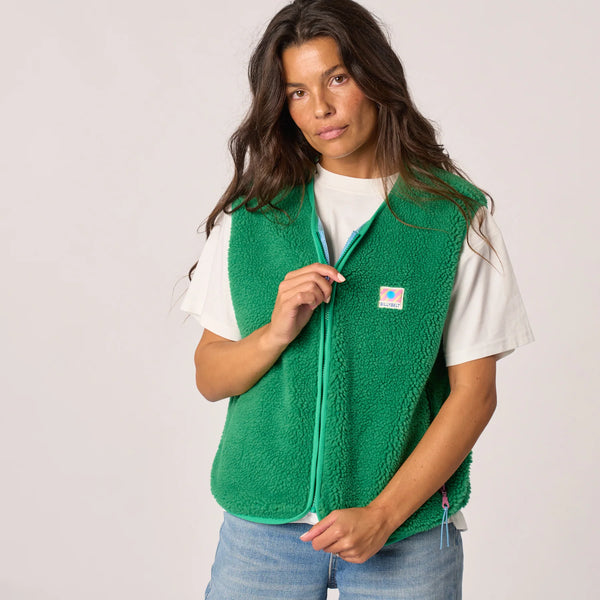 Woman wearing a green fleece vest with a visible brand logo on a plain background