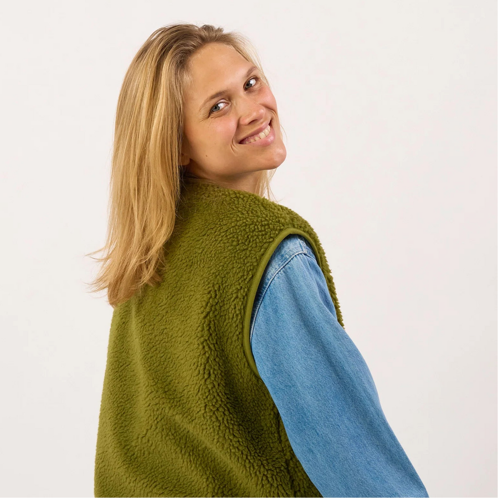 Person wearing a green fleece vest over a blue shirt on a white background