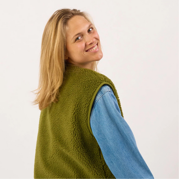 Person wearing a green fleece vest over a blue shirt on a white background