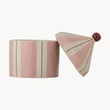 A pink and cream striped ceramic container with its matching lid leaning against it, set against a plain off-white background.