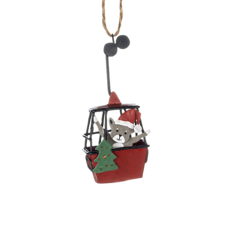 Christmas ornament of a cat in a red cable car with a Santa hat and green tree, on a white background.