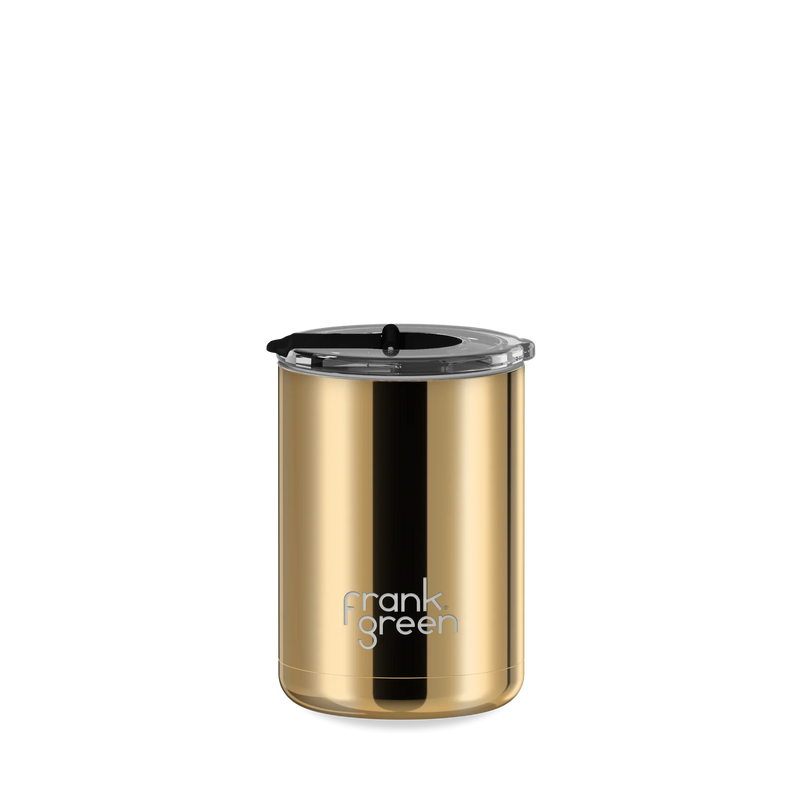 A gold stainless steel travel tumbler with a black lid and a black vertical accent stripe, featuring the 'frank green' logo near the bottom, set against a plain white background.