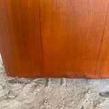 Close-up of a reddish-brown wooden panel or furniture corner resting on a rough concrete floor.