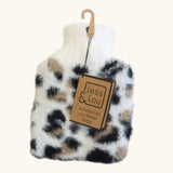 A plush faux-fur hot water bottle with an animal print pattern in black, beige, and white, hanging from a wooden hanger with a paper tag that reads 'Jess & Lou'.