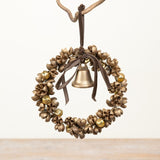 A rustic metal jingle wreath ornament with a small brass bell in the center, hanging from a branch against a plain light background.