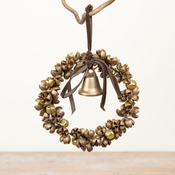 A rustic metal jingle wreath ornament with a small brass bell in the center, hanging from a branch against a plain light background.