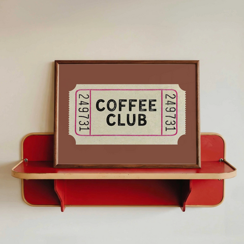 Dandy Prints - A framed art print featuring a vintage-style coffee club ticket with the words 'COFFEE CLUB' in black on an off-white background, mounted on a red wall shelf against a light beige wall.