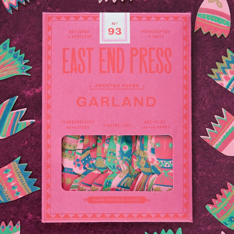East End Press No. 93 Garland printed paper box in pink, showing colorful patterned paper rolls inside a window, set against a dark purple textured background with decorative paper cutouts.