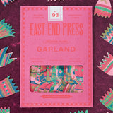 East End Press No. 93 Garland printed paper box in pink, showing colorful patterned paper rolls inside a window, set against a dark purple textured background with decorative paper cutouts.