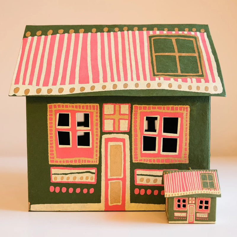A hand-painted folk art house figurine with a dark green body, pink and white striped roof, and gold accents, shown next to a smaller matching house on a beige background.
