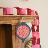 Decorative paper chain with pink and blue hanging ornaments on a wooden surface.