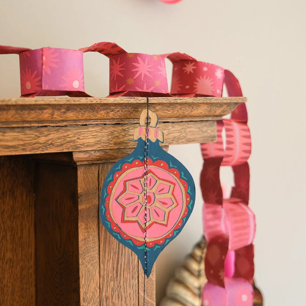 Decorative paper chain with pink and blue hanging ornaments on a wooden surface.
