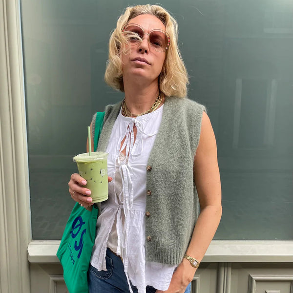 Woman holding a green drink and a green bag against a gray wall.