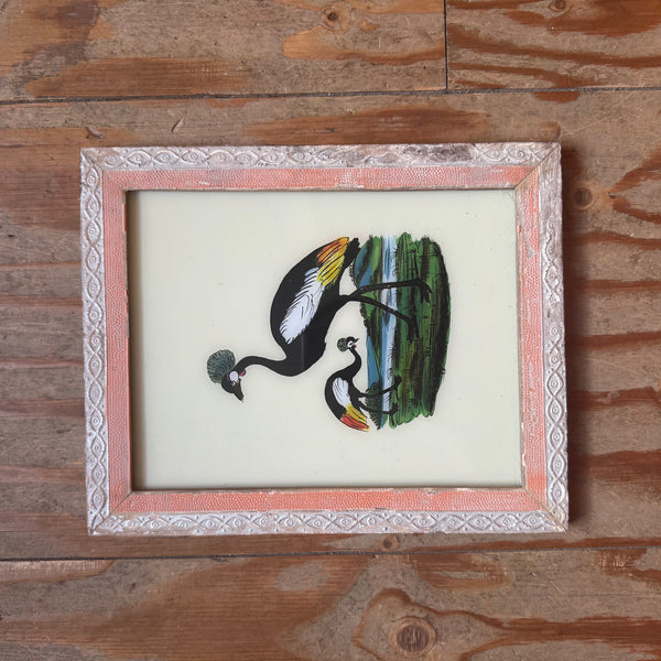 Framed artwork of two peacocks on a wooden surface