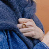 A close-up of a person wearing a textured blue fuzzy wrap or scarf, with a gold ring on one finger, against a warm orange wall.