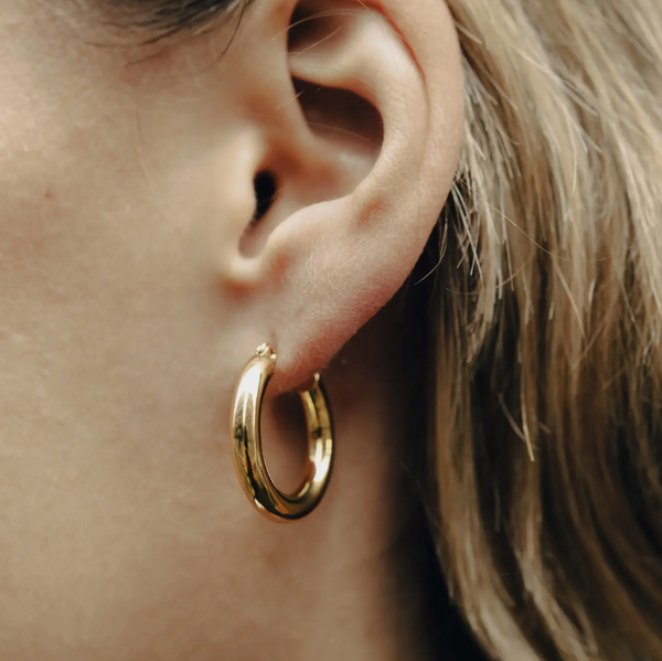 A close-up image of a person wearing a gold classic hoop earring.