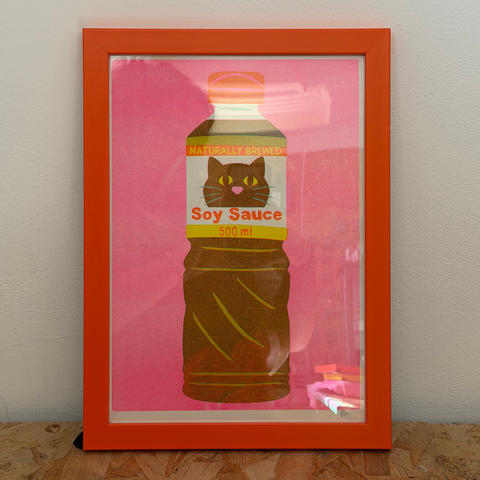 Framed artwork of a soy sauce bottle with a cat illustration on a pink background.