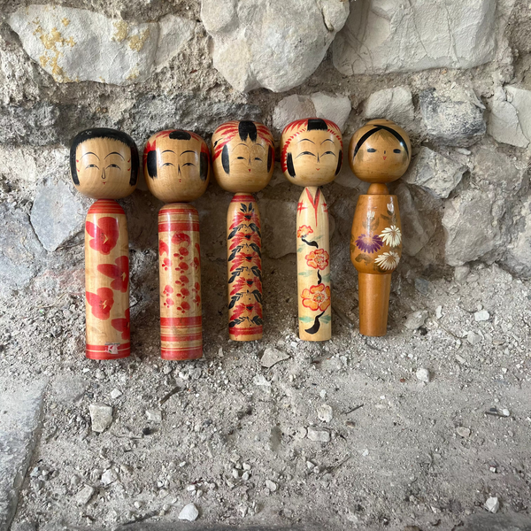 Set of five wooden kokeshi dolls against a stone wall.