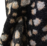 Close-up of a fuzzy knit fabric with a black base and irregular beige and light gray spots, shown with soft folds.