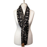 A black fuzzy scarf with a beige and gray spotted pattern, draped on a white mannequin torso against a white background.